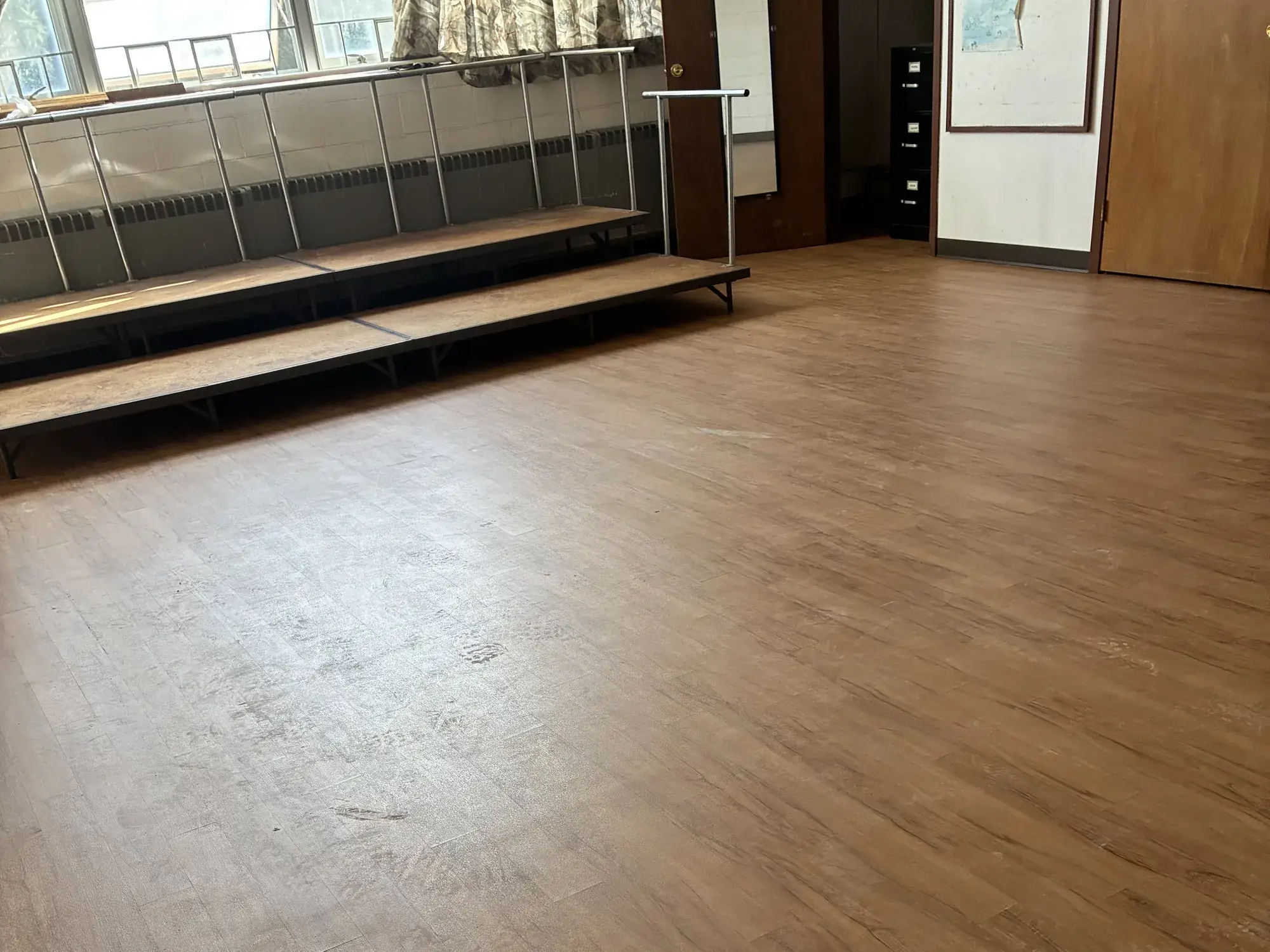 A meeting hall with newly installed wood-look vinyl plank flooring in front of a low stage